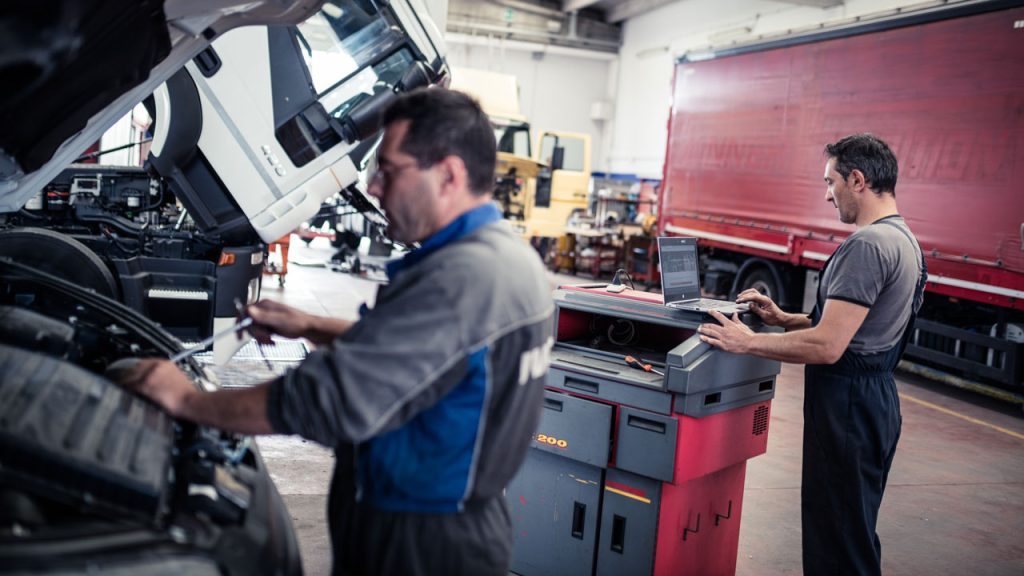 Two mechanics in a truck repair workshop using technical data from Atelio Data Truck