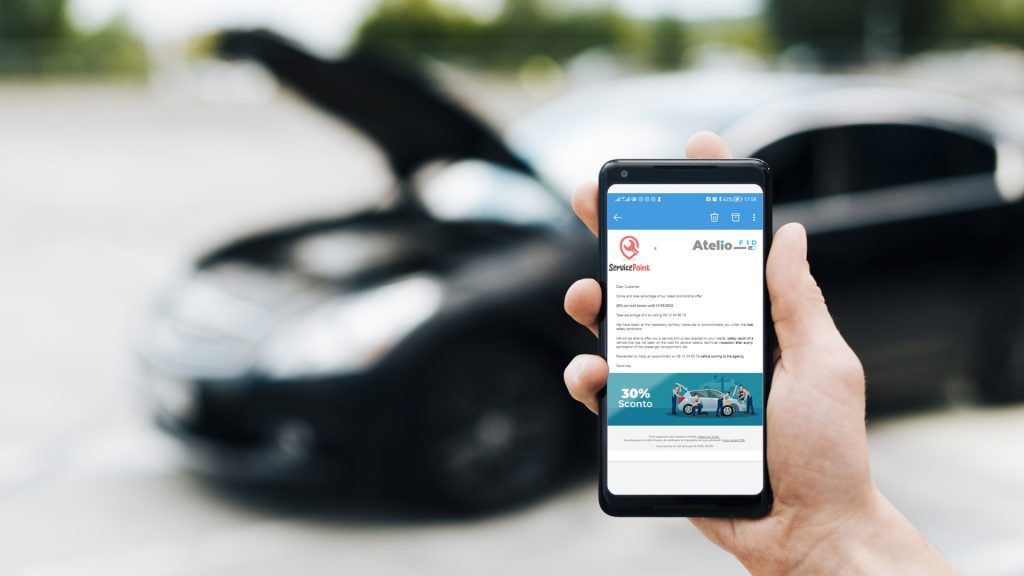 Mano tiene in mano un cellulare che mostra una email ricevuta grazie ad atelio fid software di marketing per officine