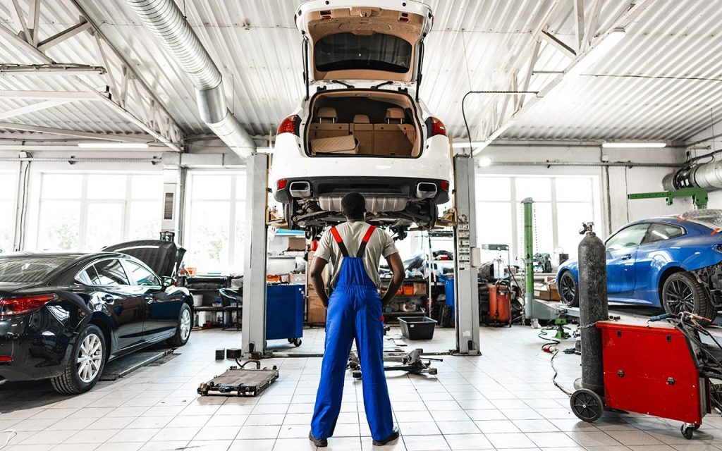 pensieroso giovane meccanico che guarda l'auto pensando a quanto tempo serve per ripararla
