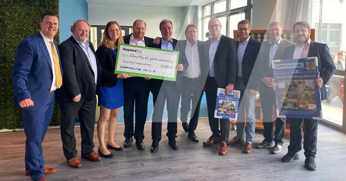 A group photograph of HaynesPro and TOPMOTIVE holding a cheque for a donation to celebrate 20 years of collaboration.