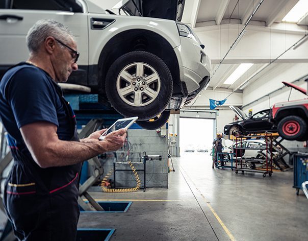 Meccanico auto in officina che sta consultando i dati tecnici da un tablet con i software di Infopro Digital Automotive per le officine auto, fast fit e gommisti