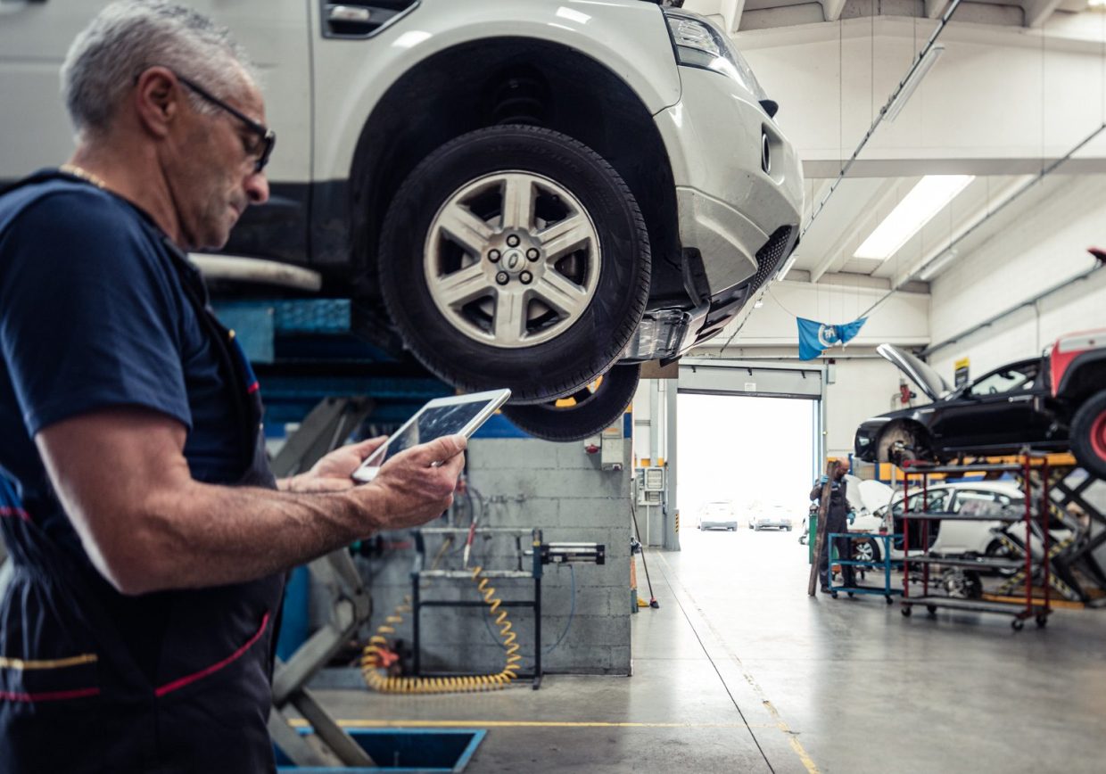 Meccanico auto in officina che sta consultando i dati tecnici da un tablet con i software di Infopro Digital Automotive per le officine auto, fast fit e gommisti
