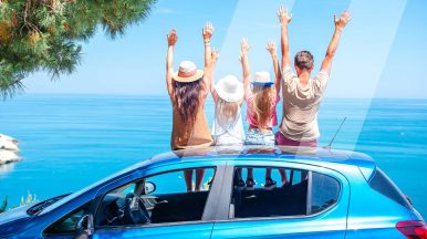 Famille assise sur le toit de leur voiture garée face à la mer pour parler de l'importance d'un check-up en atelier avant les vacances d'été