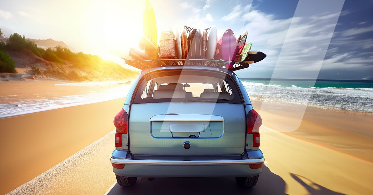 Coche circulando por la playa con maletas y tablas de surf colgando del techo